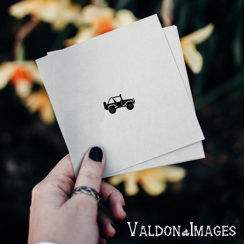 May include: A white card with a black silhouette of a jeep on it. The card is being held by a hand with black nail polish.
