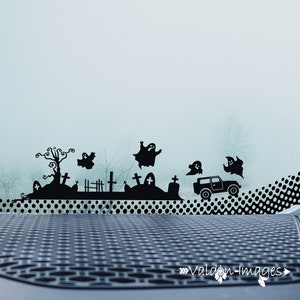 May include: A black silhouette of a graveyard with a car driving through it, ghosts flying in the air, and a dotted background. The image is a Halloween themed car decal.
