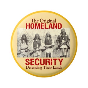 Può includere: Un bottone giallo con una foto in bianco e nero di quattro uomini nativi americani che tengono dei fucili. Il testo "The Original HOMELAND SECURITY Defending Their Lands" è stampato sul bottone.