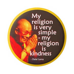 May include: A round button with a yellow border and a brown background. The button features a photo of the Dalai Lama with the quote "My religion is very simple - my religion is kindness - Dalai Lama".