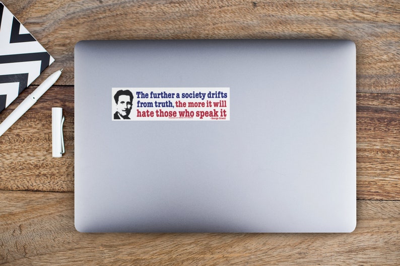 May include: A rectangular sticker on a laptop with a quote by George Orwell. The text reads: "The further a society drifts from truth, the more it will hate those who speak it." The sticker has a portrait of a man.