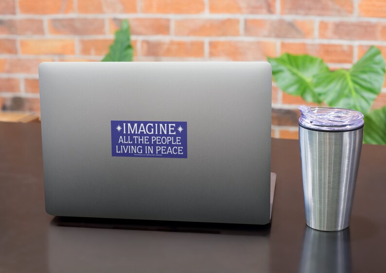 May include: A blue sticker with white text on a silver laptop. The sticker says "*IMAGINE* ALL THE PEOPLE LIVING IN PEACE".