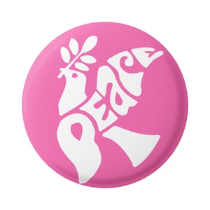 Può includere: Un bottone rosa con una colomba bianca che porta un ramo di ulivo e la parola "pace" scritta nel corpo della colomba.