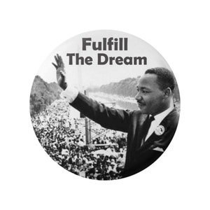 May include: Black and white photo of Martin Luther King Jr. giving a speech. He is standing on a stage with a large crowd behind him. The text "Fulfill The Dream" is written above him.