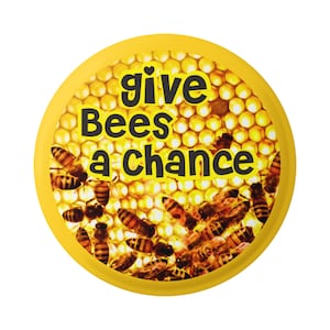 May include: Yellow button with a honeycomb pattern and bees. The text "give Bees a chance" is printed in black.