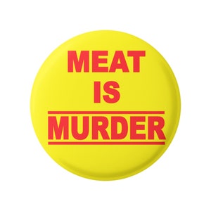 Puede incluir: Un botón amarillo con el texto "MEAT IS MURDER" en letras rojas.