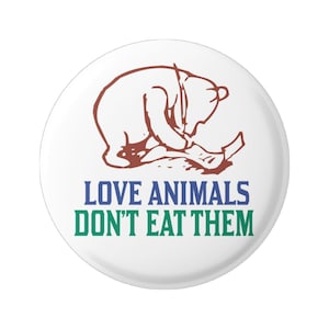 Może przedstawiać: Biały guzik z brązowym rysunkiem liniowym przedstawiającym niedźwiedzia siedzącego z kawałkiem papieru w łapkach. Tekst "LOVE ANIMALS DON'T EAT THEM" jest napisany niebieskimi i zielonymi literami.