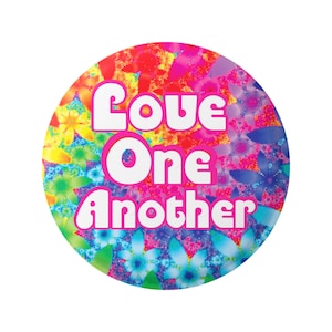 Könnte beinhalten: Ein runder Knopf mit einem bunten Blumenmuster und dem Text "Love One Another" in weißen Buchstaben mit rosa Umrandung.