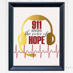 Op de afbeelding: Ingelijste print met een zwarte rand. Het kunstwerk toont een gouden headsetvorm met de woorden "911 DISPATCHERS the voice of HOPE" in rood en zwart. Een rode hartslaglijn loopt over de bodem.