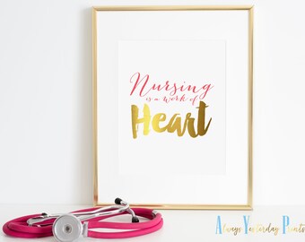 May include: A gold framed print with the text "Nursing is a work of Heart" in pink and gold lettering. A pink stethoscope is in the foreground.