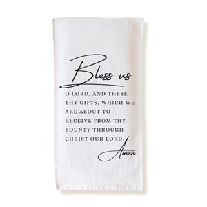May include: White rectangular kitchen towel with the words "Bless us" in a script font. Below, the text reads "O LORD, AND THESE THY GIFTS, WHICH WE ARE ABOUT TO RECEIVE FROM THY BOUNTY THROUGH CHRIST OUR LORD. Amen."