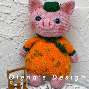 May include: A handmade crochet pig doll with a pumpkin-themed outfit. The pig is pink with blue eyes and wears an orange and green outfit. The image includes a miniature pumpkin patch stand and small pumpkin decorations.