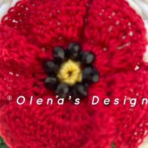 May include: Close-up of a handmade red crocheted flower with a yellow center and black bead accents. The flower is part of a larger design, with the text "Olena's Design" visible.