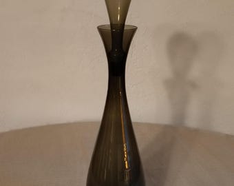 May include: A tall, dark gray glass decanter with a matching stopper. The decanter has a rounded bottom and a narrow neck.