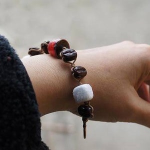 May include: A bracelet with brown, red, and white beads. The bracelet is made of coffee beans and other materials.
