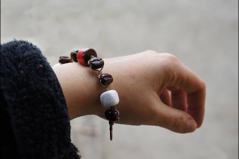 May include: A bracelet with brown, red, and white beads. The bracelet is made of coffee beans and other materials.
