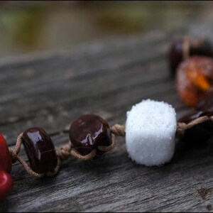 May include: A close-up of a brown and white beaded necklace with a red ceramic cup charm. The beads are made of wood and have a natural finish. The necklace is strung on a brown cord.