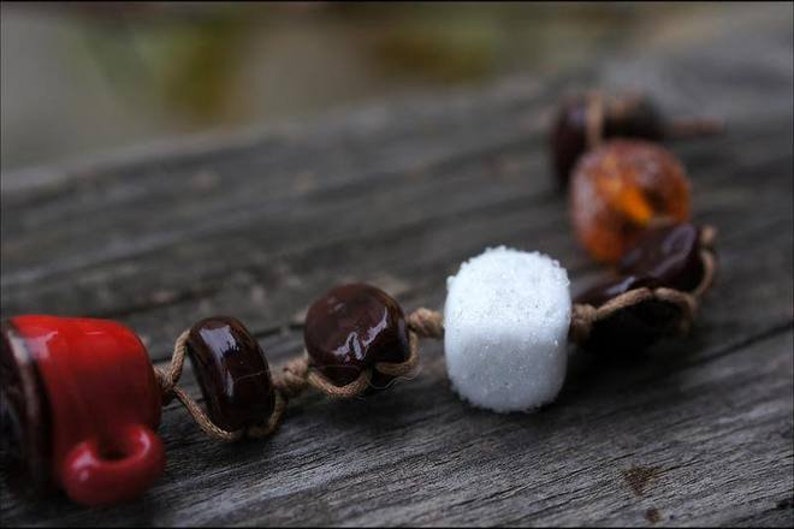 May include: A close-up of a brown and white beaded necklace with a red ceramic cup charm. The beads are made of wood and have a natural finish. The necklace is strung on a brown cord.