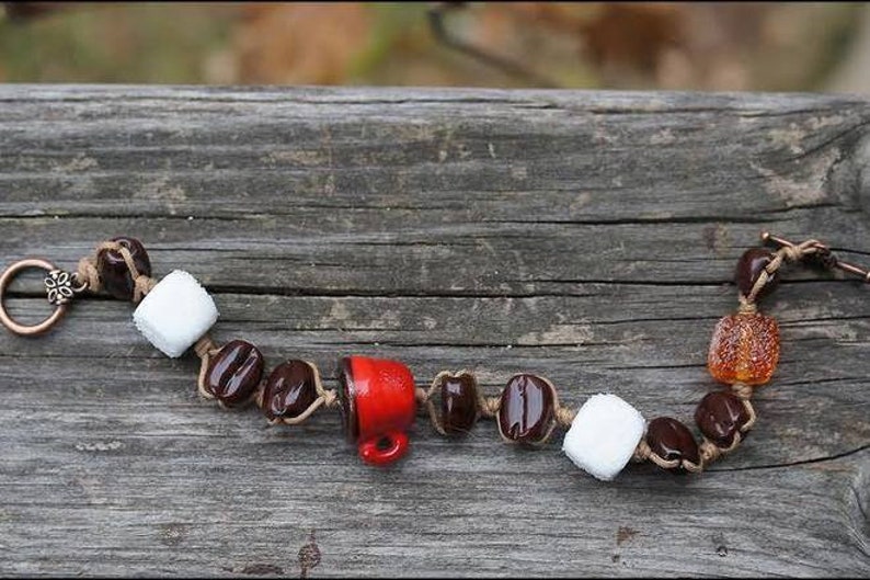 May include: A brown leather bracelet with brown, white, and red beads. The beads are shaped like coffee beans, marshmallows, and a coffee cup.