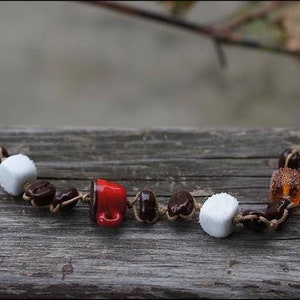May include: A brown leather bracelet with white and brown ceramic beads, a red ceramic coffee cup charm, and a brown and orange glass bead.