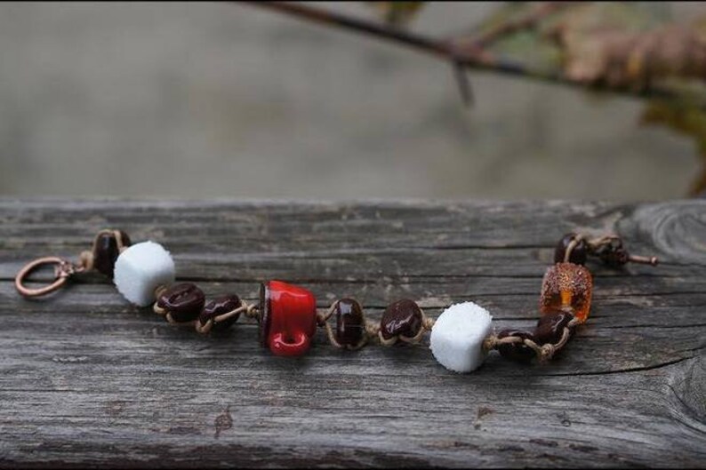 May include: A brown leather bracelet with white and brown ceramic beads, a red ceramic coffee cup charm, and a brown and orange glass bead.