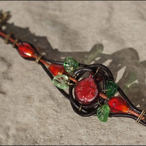 Op de afbeelding: Een leren armband met rode en groene glazen kralen, een rode glazen granaatappel en een messing sluiting.