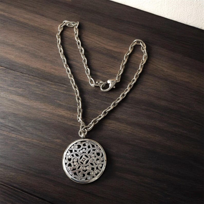 May include: Silver-toned necklace with a round pendant featuring an openwork floral design. The chain is a chunky link style with a lobster clasp closure. The pendant is approximately 2 inches in diameter.