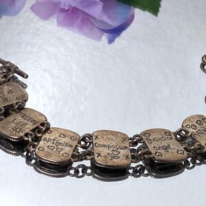 Puede incluir: Una pulsera de eslabones de metal plateado con siete dijes rectangulares. Cada dije est&aacute; grabado con palabras como Dream, Tree of Life, Optimism, Compassion, Guardian Angel, Harmony, Love and Respect y Truth, junto a peque&ntilde;os s&iacute;mbolos.