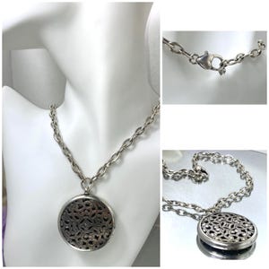 May include: Silver-toned necklace with a large, round pendant. The pendant features an intricate openwork design. The chain is a chunky link style, and the necklace is displayed on a white mannequin bust.