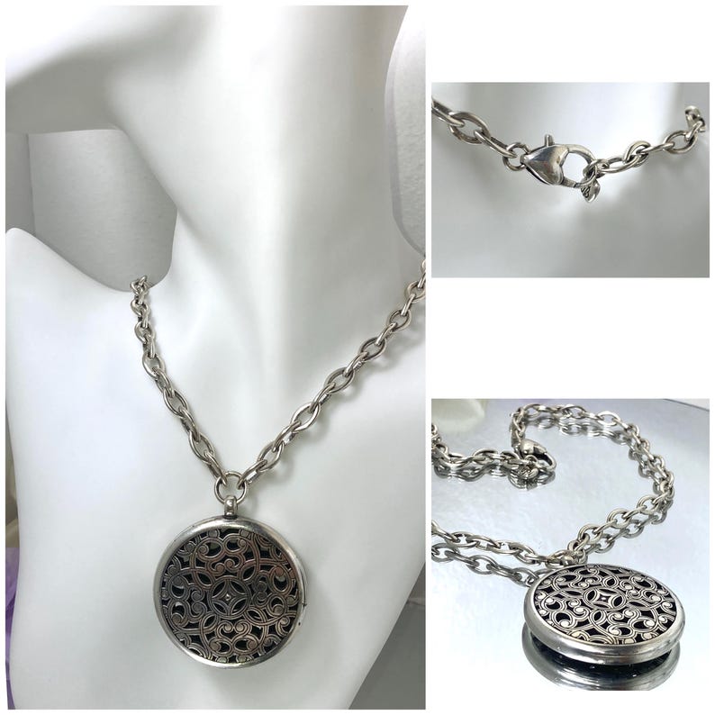 May include: Silver-toned necklace with a large, round pendant. The pendant features an intricate openwork design. The chain is a chunky link style, and the necklace is displayed on a white mannequin bust.