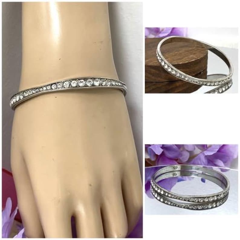 Puede incluir: Una pulsera r&iacute;gida de metal en tono plateado que presenta una hilera continua de pedrer&iacute;a transparente de corte redondo incrustada en la superficie exterior. La pulsera tiene un acabado pulido y un perfil circular delgado y uniforme.