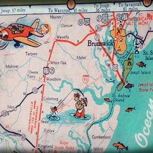 May include: A vintage map of the Brunswick, Georgia area with a red airplane flying over the top. The map shows the location of Brunswick, St. Simons Island, Jekyll Island, and other nearby towns. The map also includes distances between towns and points of interest.