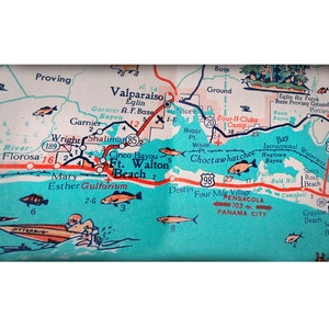 May include: A vintage map of the Florida panhandle with a turquoise blue background and red and white markings. The map shows the location of cities, towns, and points of interest, including Pensacola, Panama City, and Fort Walton Beach. The map also includes a small illustration of a boat with the word "JITTERBUG" written on it.