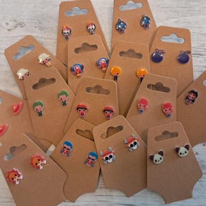 May include: Assortment of colorful cartoon character earrings displayed on brown card stock. The earrings are made of polymer clay and feature various characters from popular anime and manga series.