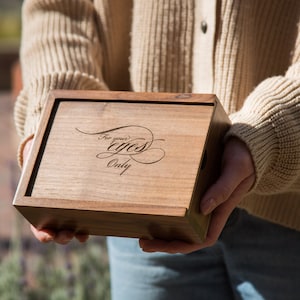 May include: A wooden box with the words "For your eyes only" engraved on the top. The box is being held by a person wearing a beige sweater.