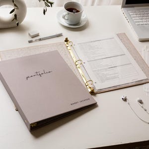 May include: A white ceramic mug with a black handle and the text "But First, Coffee" in a bold, black font. The mug is set against a blurred background, suggesting a cozy setting.