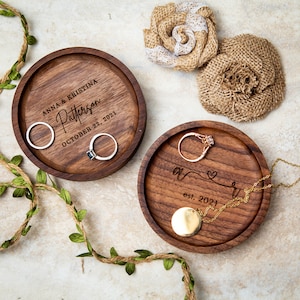 May include: Two wooden ring dishes with engraved text. The first dish says "Anna & Kristina Patterson October 22, 2021". The second dish says "A & R est. 2021" with a heart symbol.