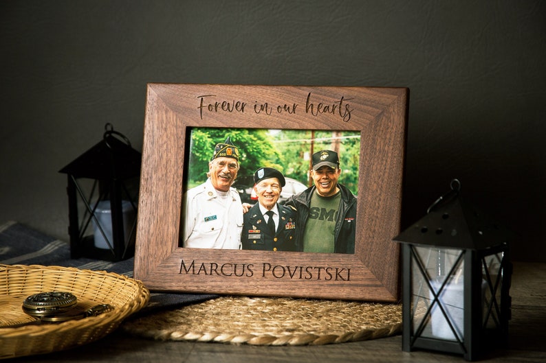 Op de afbeelding: Een houten fotolijst met een foto van drie mannen. De lijst is gegraveerd met de woorden "Forever in our hearts" en "Marcus Povistski".