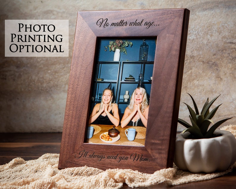 Op de afbeelding: Een donkerbruin houten fotolijst met een foto van twee lachende vrouwen. De lijst heeft een gegraveerd bericht met de tekst "Het maakt niet uit hoe oud... Ik heb je altijd nodig, Mam."