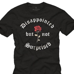 Può includere: T-shirt nero con la scritta "Disappointed but not Surprised" in carattere gotico, con una grafica di rosa rossa. La maglietta ha maniche corte e girocollo.