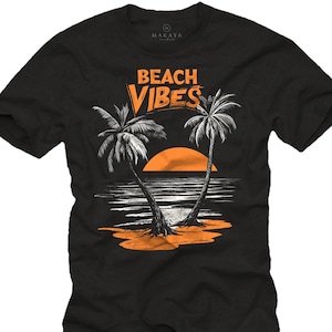 May include: Black t-shirt with an orange and white graphic. The graphic features two palm trees, a setting sun, and the words "BEACH VIBES" in orange. The shirt is made of a soft material.