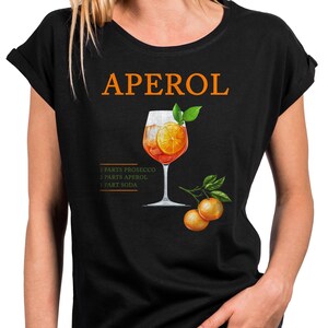 Könnte beinhalten: Schwarzes T-Shirt mit einem Aperol Spritz Rezept-Grafik. Das Design beinhaltet das Wort "APEROL" in Orange, eine Cocktail-Illustration mit einer Orangenscheibe und das Rezept: 3 Teile Prosecco, 2 Teile Aperol und 1 Teil Soda.