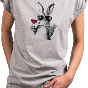May include: A gray t-shirt featuring a black and white illustration of a rabbit wearing sunglasses and holding a glass of red wine. The rabbit graphic is centered on the shirt.