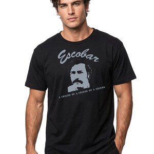 May include: Black t-shirt featuring a gray portrait and the name "Escobar". Below the portrait, the text reads "A FRIEND OF A FRIEND OF A FRIEND". The shirt has short sleeves and a crew neck.