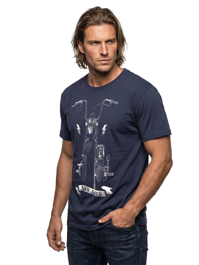 Puede incluir: Camiseta azul marino con un gr&aacute;fico detallado de una motocicleta, rayos y el texto "BAD SEED" en una pancarta. La camiseta se combina con vaqueros azules.
