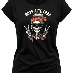 K&ouml;nnte beinhalten: Schwarzes T-Shirt mit einem Skelett, das eine Sonnenbrille und ein rotes Bandana tr&auml;gt und das Peace-Zeichen zeigt. Der Text "B&Ouml;SE ALTE FRAU" ist &uuml;ber dem Skelett aufgedruckt. Das T-Shirt hat hochgekrempelte &Auml;rmel.