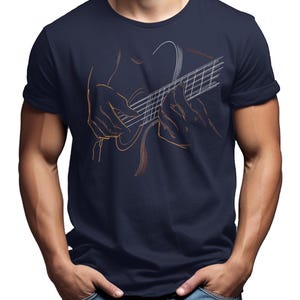 May include: Navy blue t-shirt featuring a line art illustration of a person playing a guitar. The design is in shades of orange and white, creating a striking contrast against the dark fabric. The shirt is a classic crew neck style.