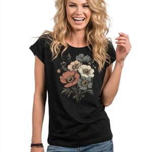 May include: Black t-shirt featuring a floral bouquet design in shades of peach, cream, and gray. The flowers are arranged with green leaves and stems. The shirt has a round neckline and short sleeves.