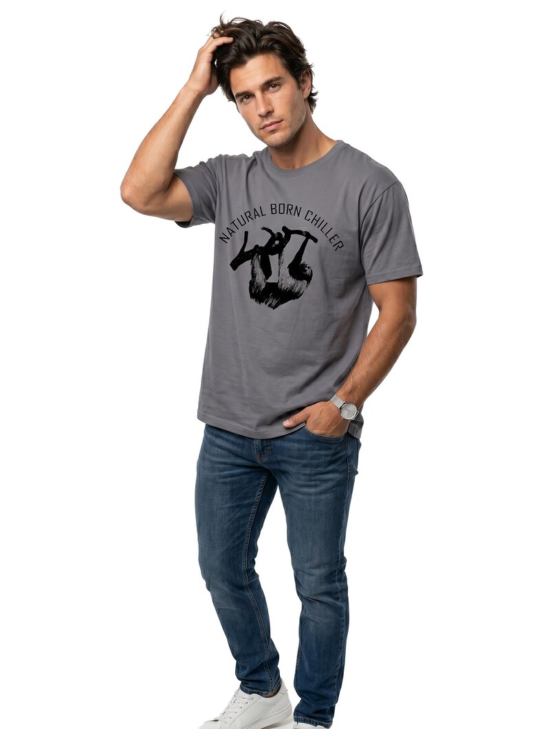 Pu&ograve; includere: T-shirt grigio con la scritta "NATURAL BORN CHILLER" e una grafica di bradipo nero. La persona indossa jeans blu e scarpe da ginnastica bianche. Un orologio d'argento &egrave; al polso.