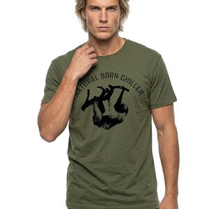 Pu&ograve; includere: T-shirt verde oliva con la scritta "NATURAL BORN CHILLER" sopra una grafica nera di un bradipo appeso a un ramo. La maglietta a maniche corte &egrave; realizzata in un materiale morbido.